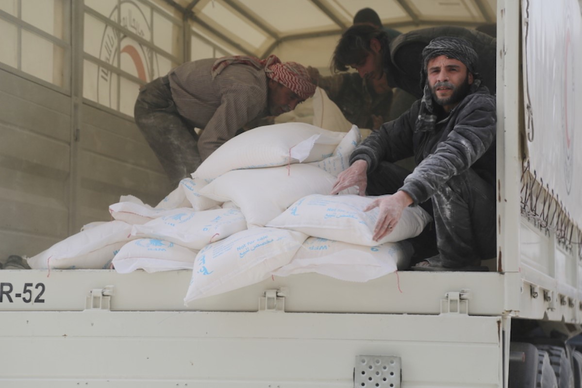 Photo: WFP/Marwa Awad  Syria, Duma, Eastern Ghouta, March, 2018, Marwa Awad, Conflict, Urban, War, Horizontal, Vehicle, Truck, Unloading, Food distribution, Sacks, Bags, Food, Men, WFP, Fortified Wheat Flour, Syrian Arab Red Crescent, SARC